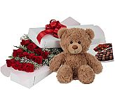 Gift box of one dozen long stemmed red roses with teddy bear and box of assorted chocolates for anniversary gift giving.