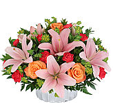 Silver reflective container with pink lilies, orange roses, pink mini carnations, and greens.