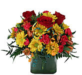 Roses, alstroemeria, asters and daisies are arranged in a rustic looking container in red, orange and yellow for dazzling birthday gift giving.