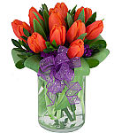 One dozen fresh and lively orange tulips in a glass vase with purple statice and purple ribbon.