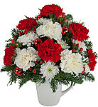 A reusable coffee mug is arranged with pretty red and white carnations, white mums, red berries, ornamental balls and holiday · greens.