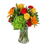 Orange lilies, yellow roses, ruby carnations and green hydrangea blossoms arranged in a clear glass cylinder vase.