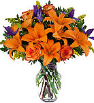 Orange roses, orange lilies, purple iris and yellow solidago arranged in a clear glass vase.
