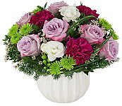 Floral arrangement in a ceramic bowl of lavender roses, wine coloured carnations, green poms, white waxflower and freesia.