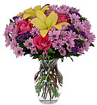 Beautiful pink roses, lavender daisies, purple statice and yellow lilies are arranged in a glass vase.