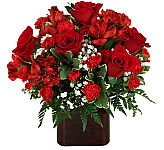 A dark red vase is arrranged with luscious red blooms including red roses, red alstroemerias and red miniature carnations.