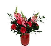 A red glass vase holds pink and red roses with pink snapdragons and assorted greenery.