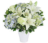 White ceramic vase of light blue hydrangea, white lilies and light green roses with greenery.