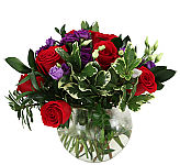 Gorgeous floral arrangement of lush red roses and dramatic purple lisianthus in a clear glass bowl.