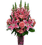 A purple tinted vase is arranged with mixed pink blooms for a funeral service. Featuring Snapdragons, Stargazer Lilies and more.