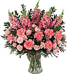 Pink snapdragons, pink carnations and pink spray roses arranged in a glass vase with added delicate flowering limonium and greens.