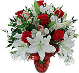 Christmas Love is a gorgeous red vased arrangement of lush red roses with white lilies and alstroemerias, seasonal greenery and candy canes, plus a red oranza bow.