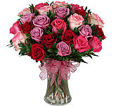 Glass vase arrangement of 24 roses in light and hot pink, red, and lavender with greens and a complimenting pink bow.