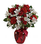 A red glass vase hold red spray roses, red carnations and white alstroemeria with lush greens, tied with a matching red ribbon.