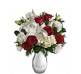 The Faith Hill Silver Noel Bouquet is a beautiful holiday arrangement of white lilies, lisianthus and hydrangea with red roses and seasonal greenery, arranged in a beautiful silver vase.