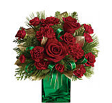 A green glass cube vase is arranged with red roses, red spray roses, red carnations, red miniature carnations, seasonal greenery, golden leaves and green ribbon.