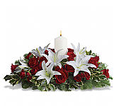 A dozen red roses, white Asiatic lilies and fresh evergreens are arranged in a dish around a white pillar candle.