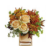 A cube vase is arranged with peach roses, bronze mums, golden disbud mums and lush greenery.